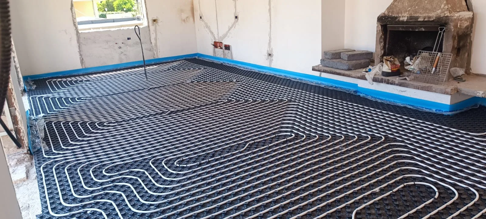 Posa dei circuiti del pavimento radiante su pannello bugnato in un soggiorno con camino, cantiere ECO-E